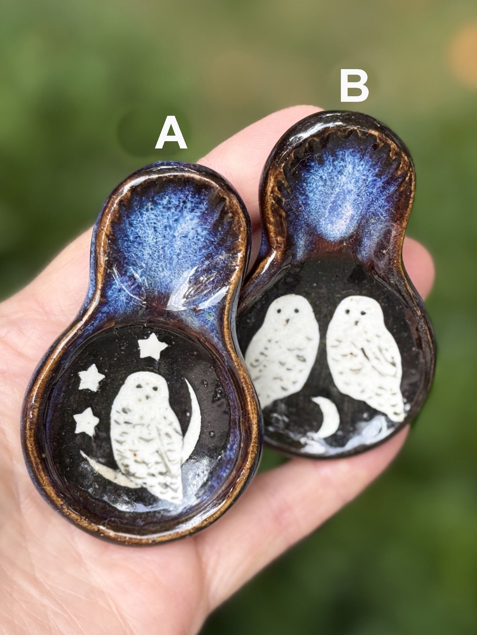 Two ceramic bowls with owl designs on a hand against a blurred green background