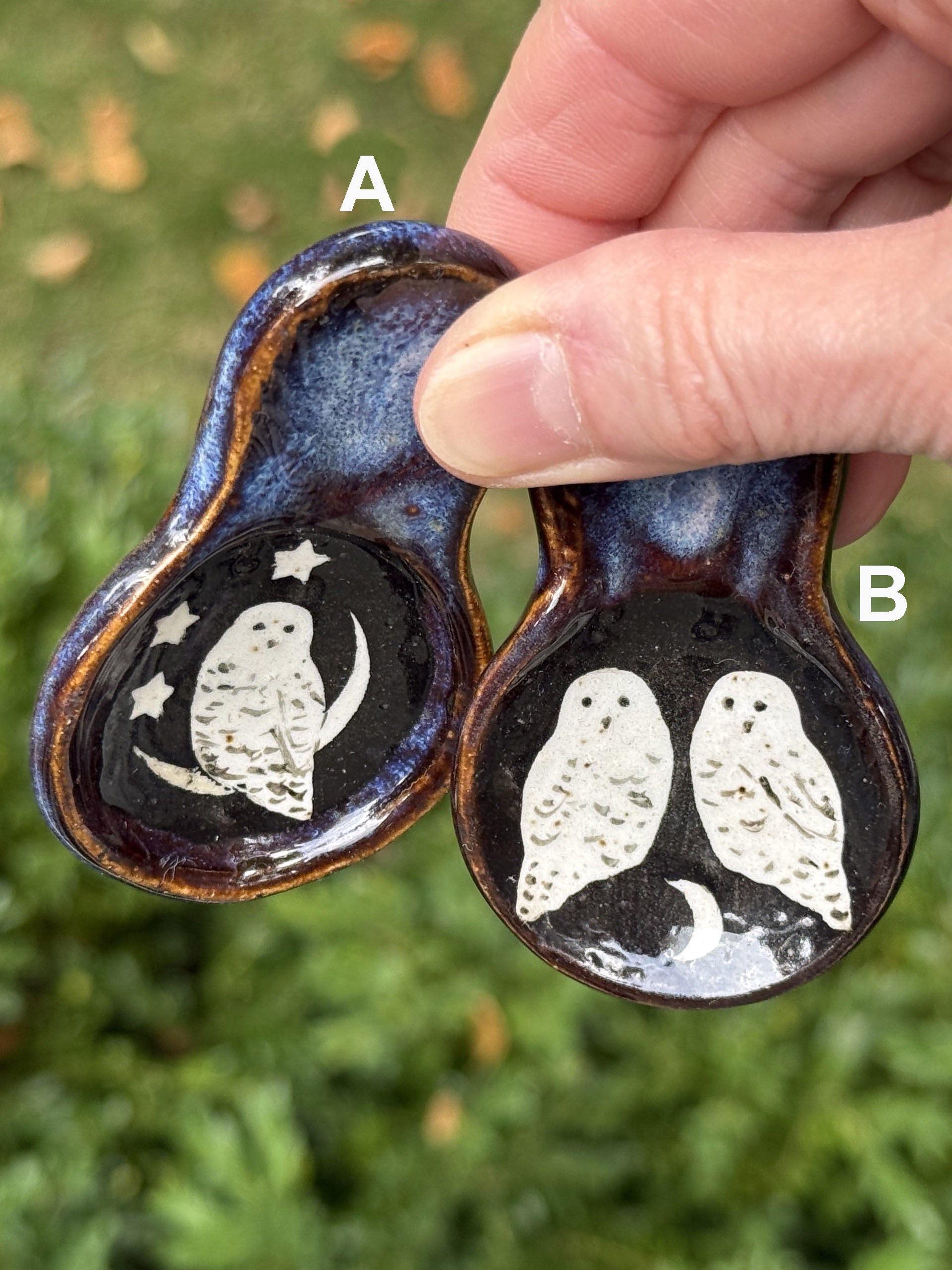 Hand holding two ceramic pieces with owl designs against a grassy background