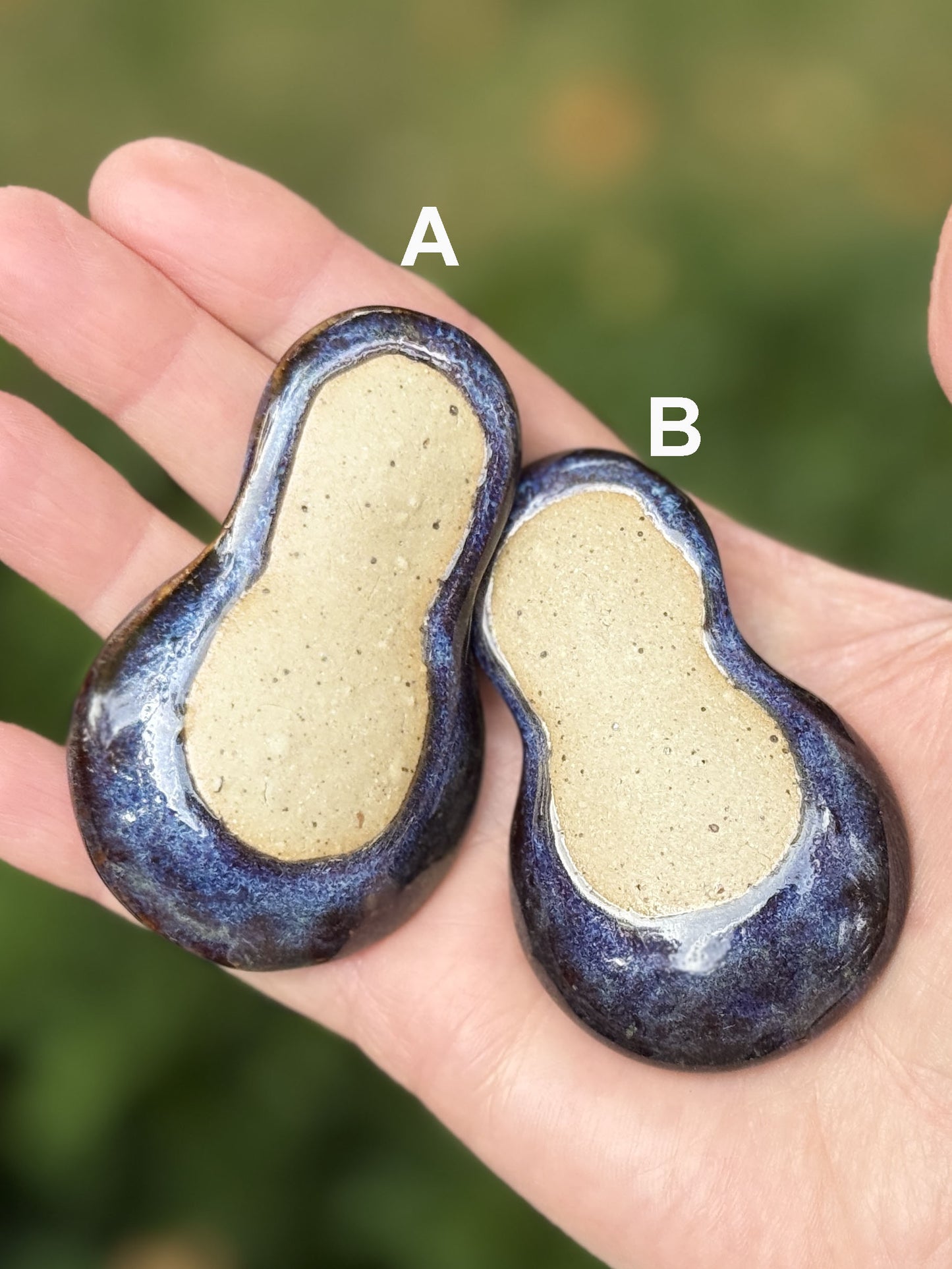 Two blue and beige ceramic objects held in a hand with a blurred green background