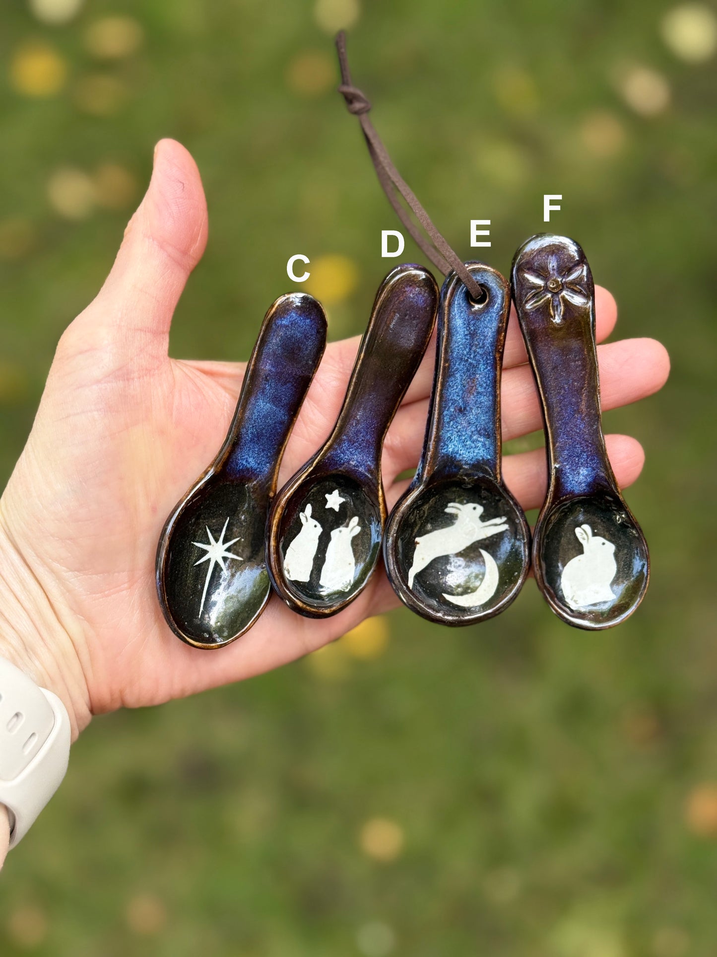 Hand holding four decorative spoons with engraved designs against a blurred natural background