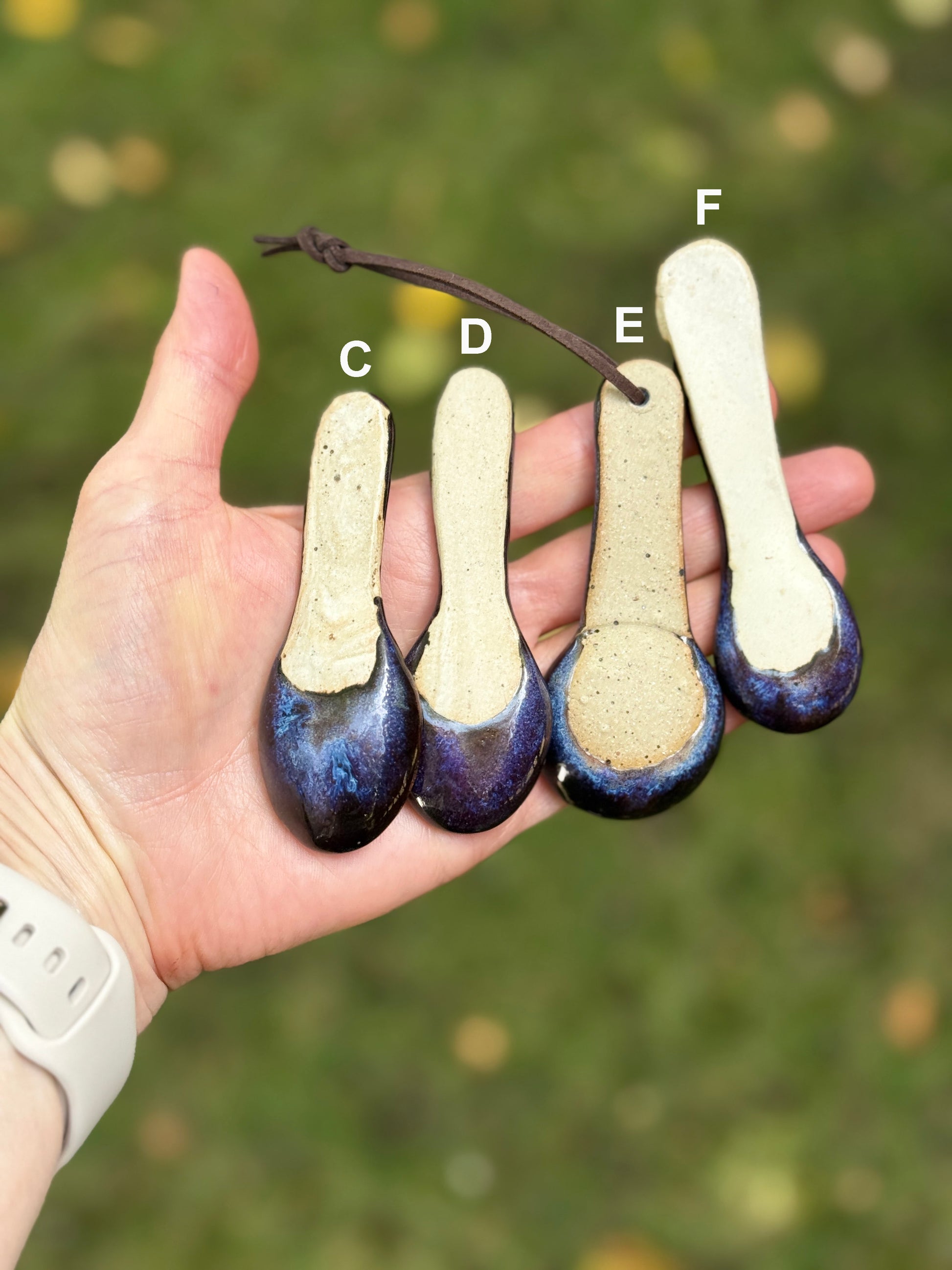 Hand holding four ceramic spoons with different designs against a blurred natural background