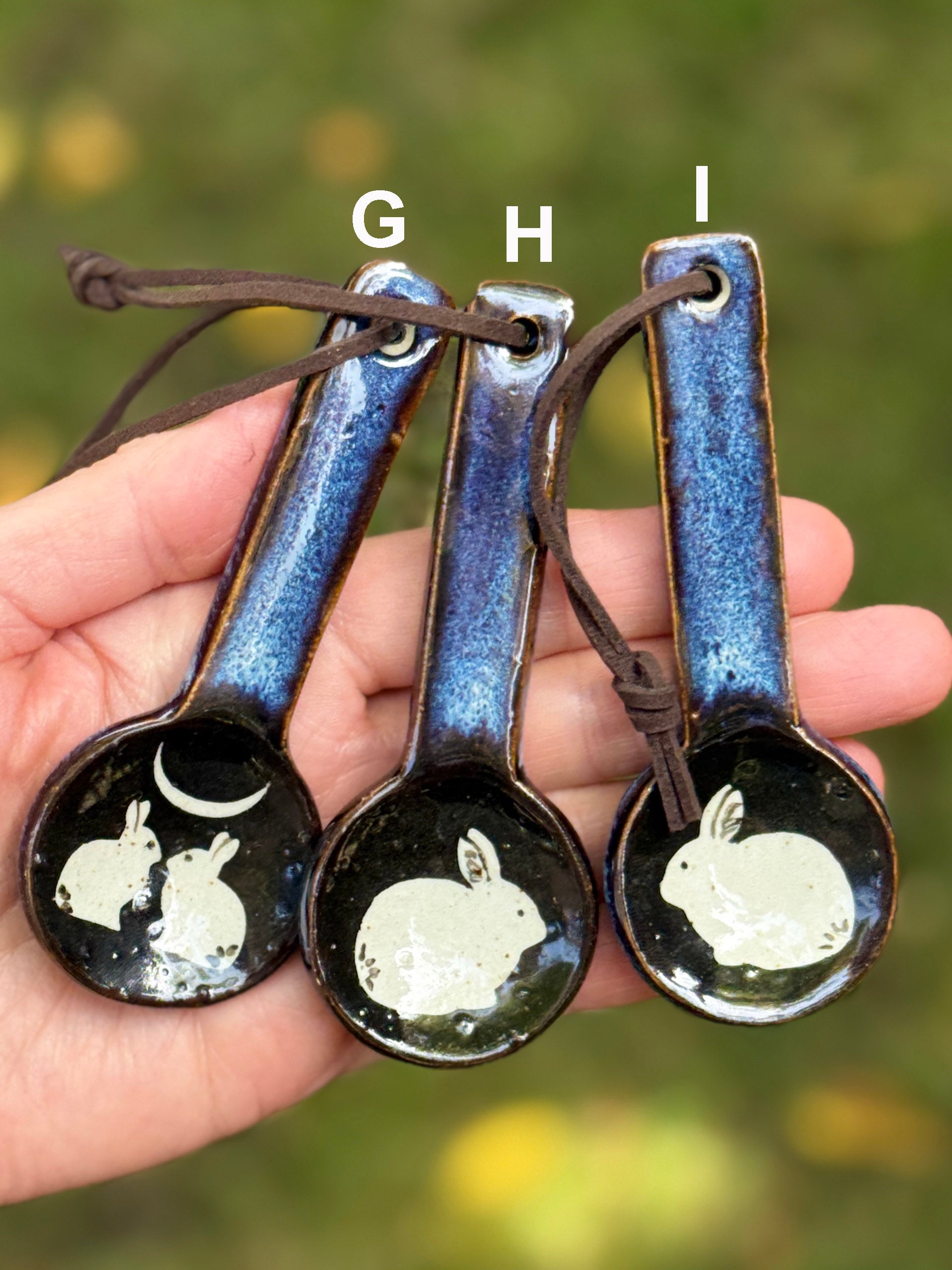 Three ceramic spoons with rabbit designs on a blurred natural background