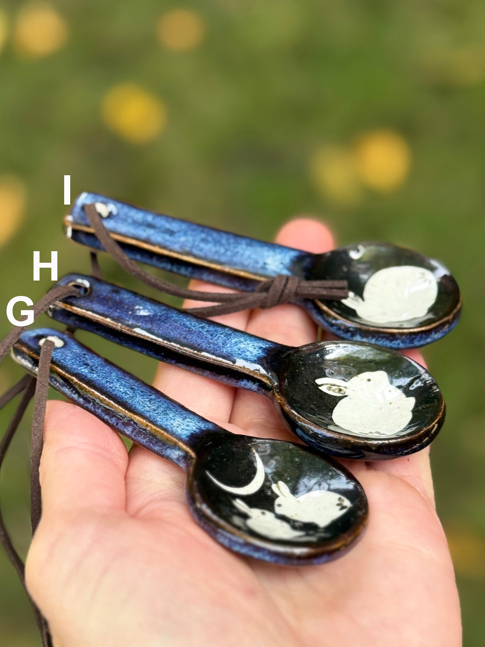 Set of decorative spoons with rabbit designs held in a hand against a blurred natural background.