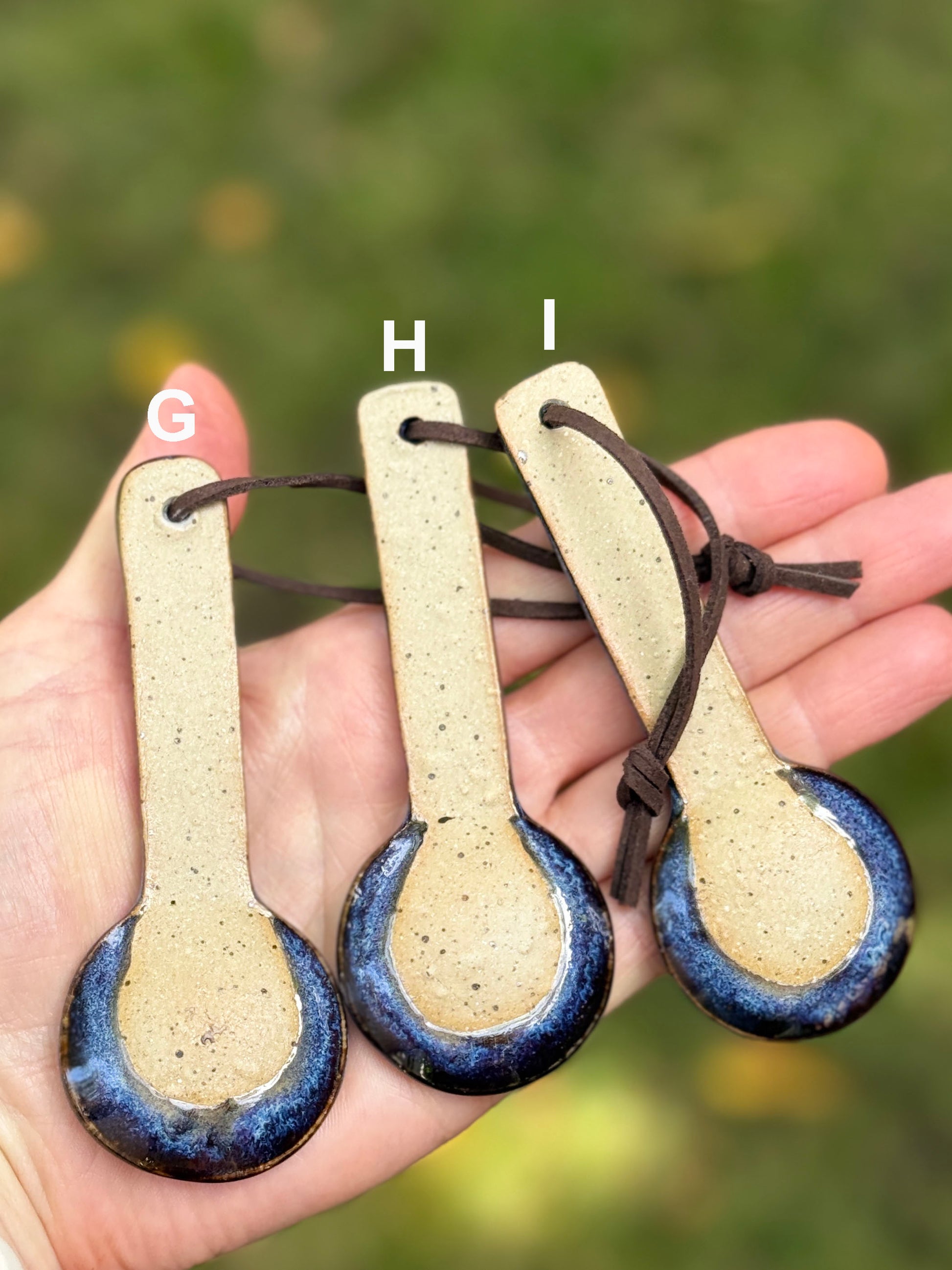 Three ceramic spoons with blue and brown bottoms held in a hand against a blurred natural background.