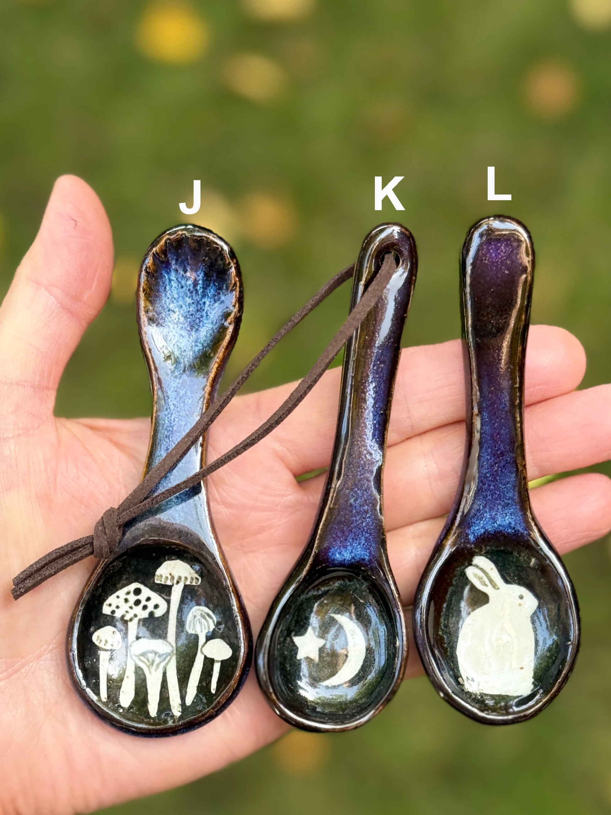 Three ceramic spoons with illustrated designs held in a hand against a blurred green background.