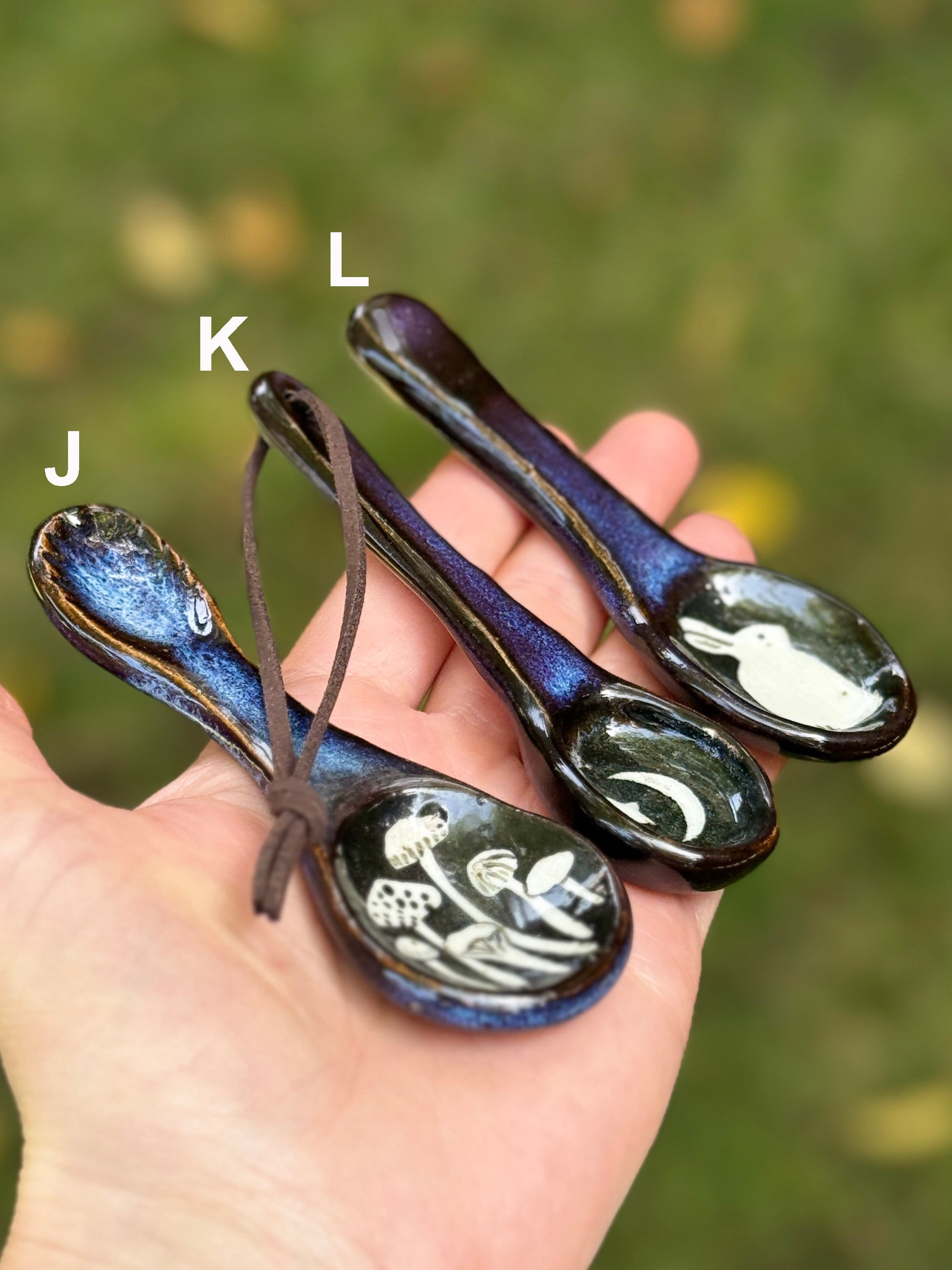 Three ceramic spoons with decorative patterns held in a hand against a blurred natural background.