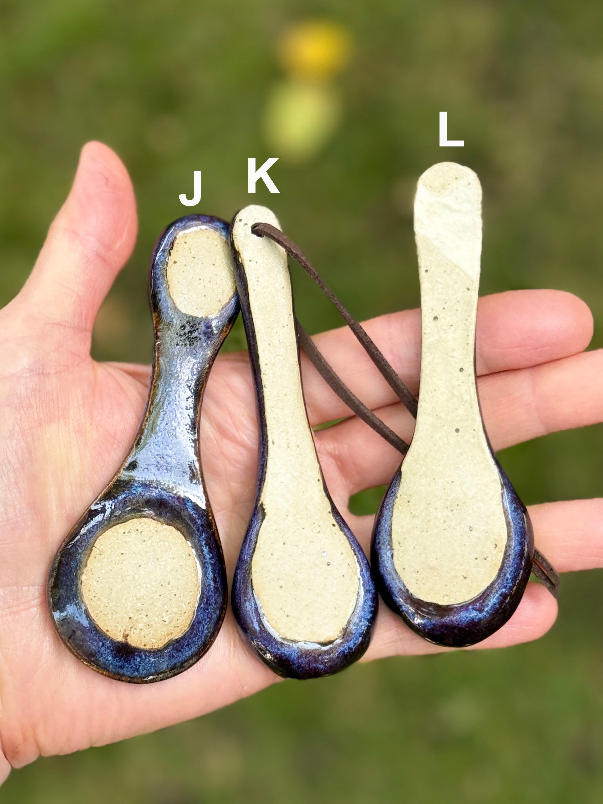 Three ceramic spoons with blue rims held in a hand against a blurred natural background.