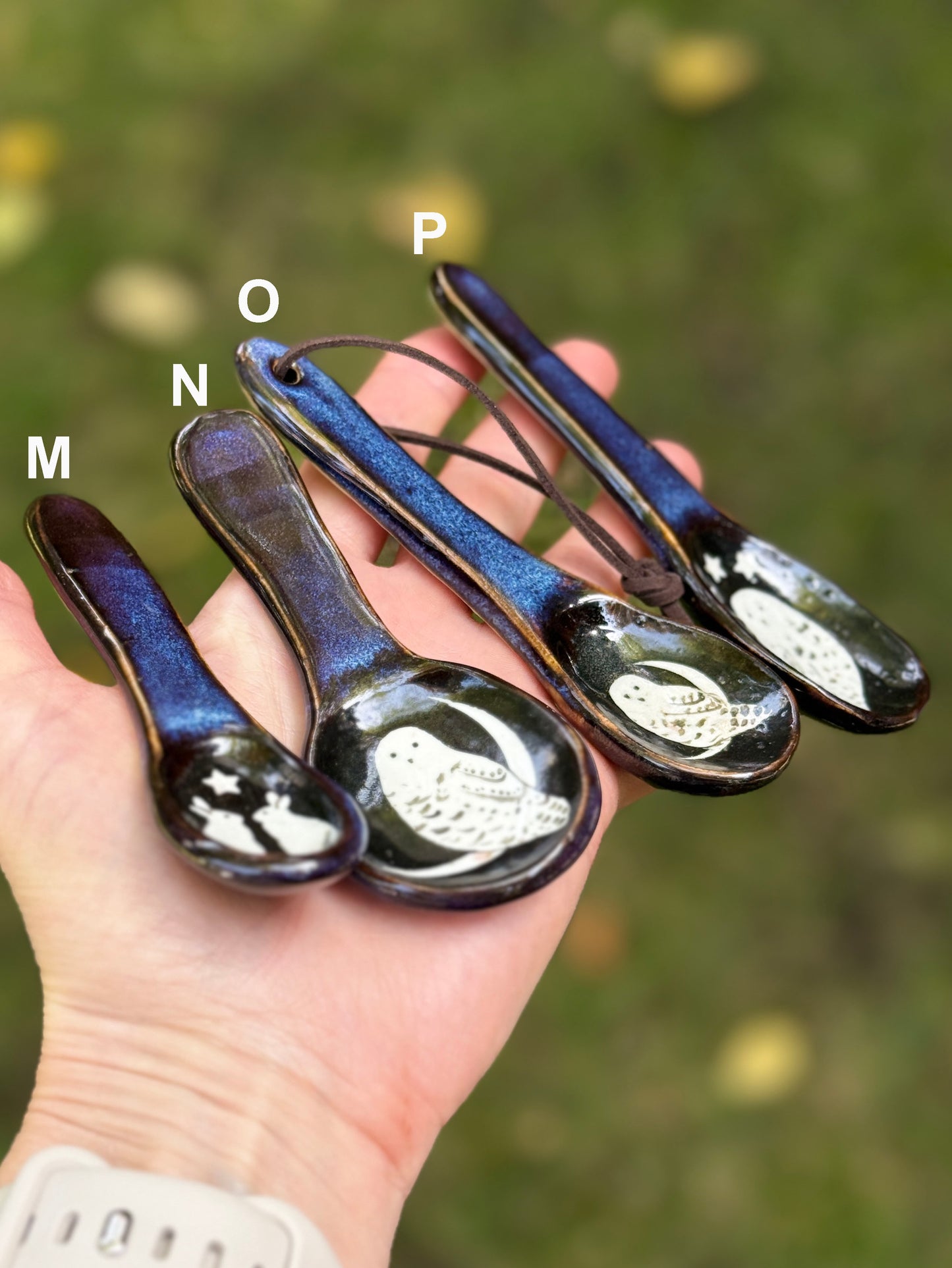 Set of four ceramic spoons held in a hand with a blurred green background