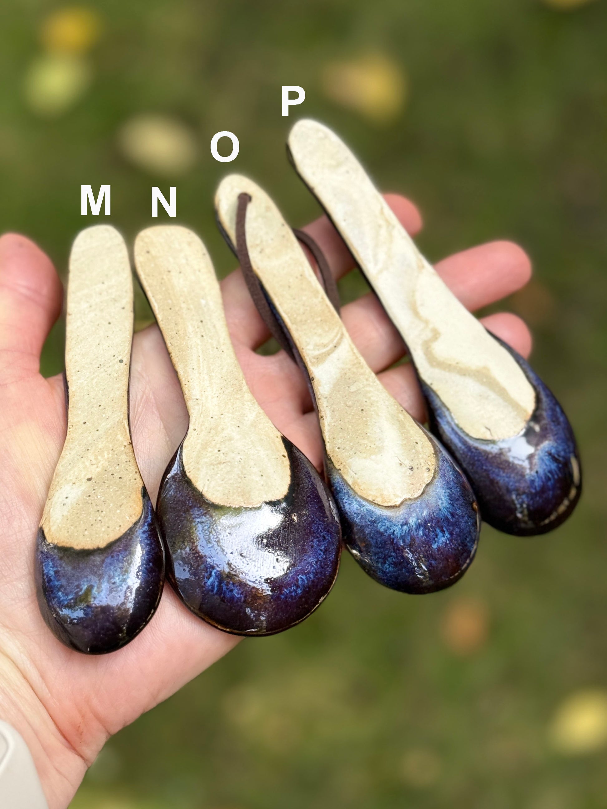 Four ceramic spoons with gradient coloring held in a hand against a blurred natural background.
