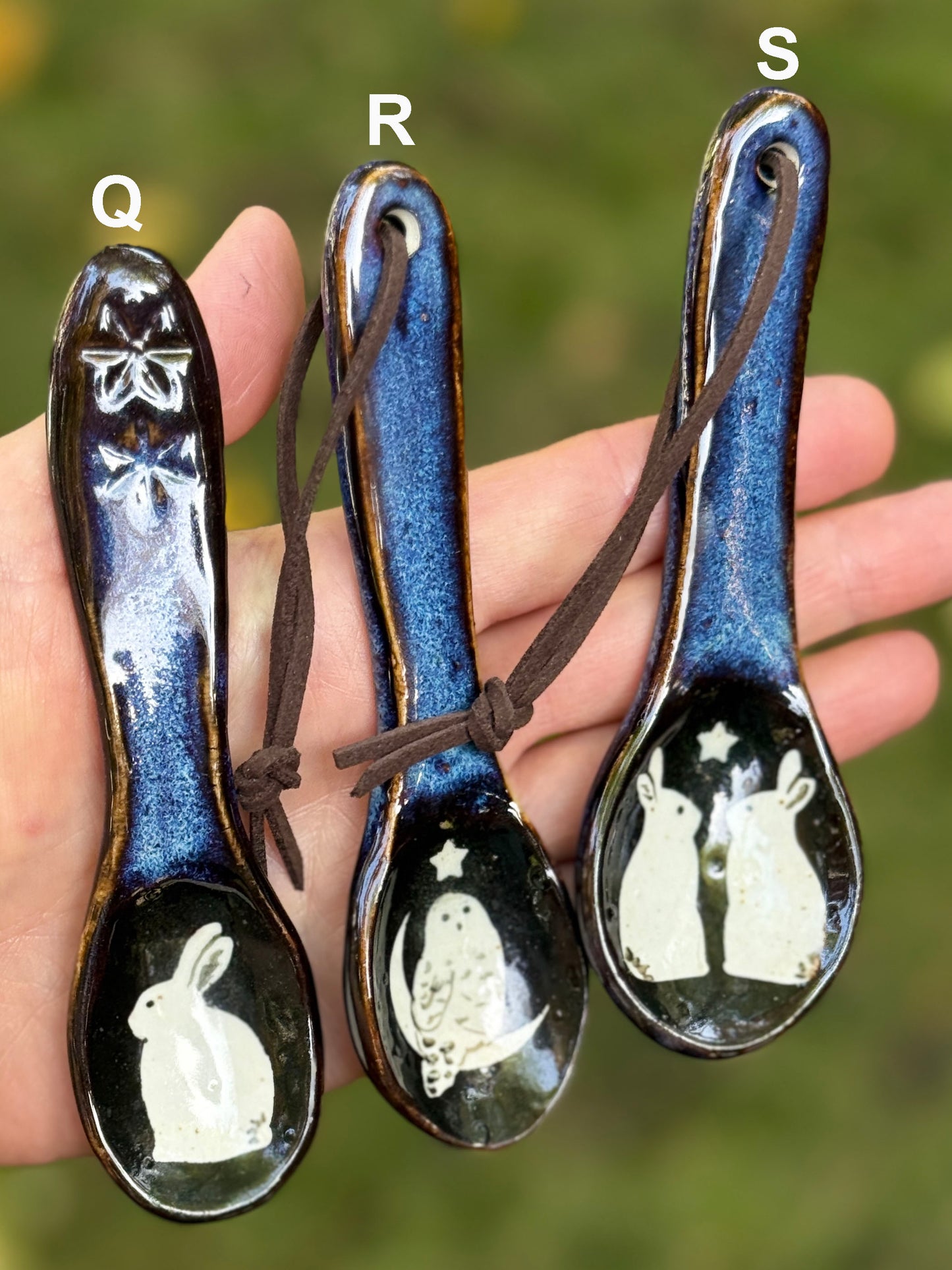 Three ceramic spoons with rabbit and owl designs held in a hand against a blurred background