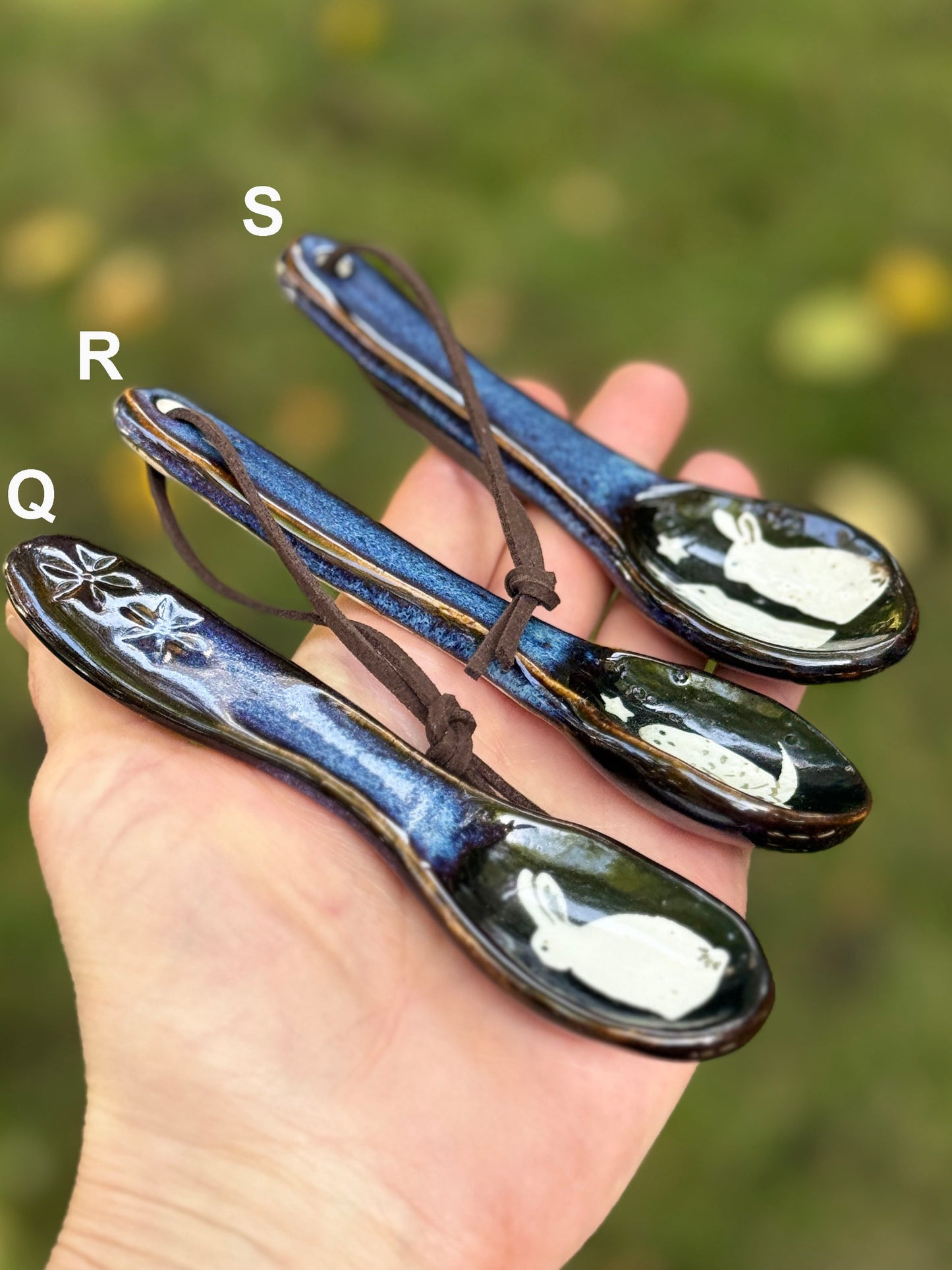 Three ceramic spoons with decorative handles held in a hand against a blurred green background.