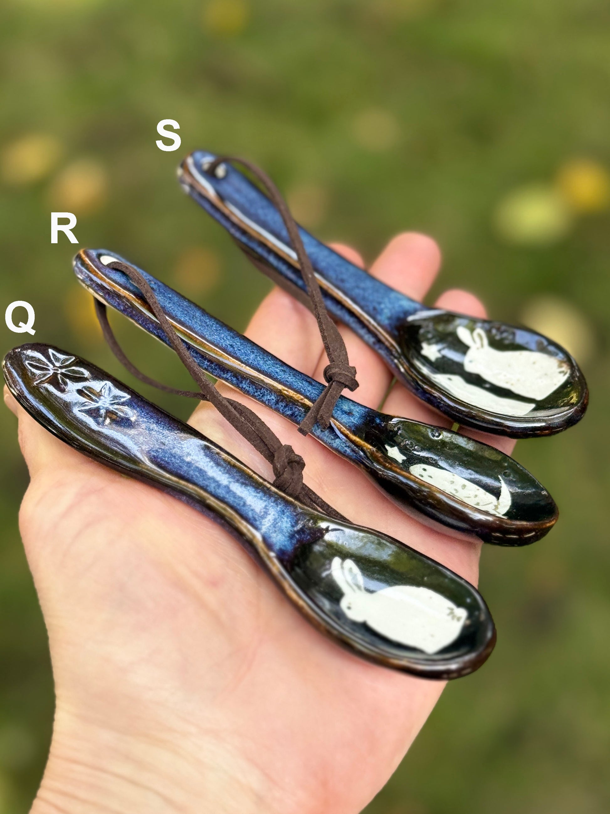 Three ceramic spoons with decorative handles held in a hand against a blurred green background.