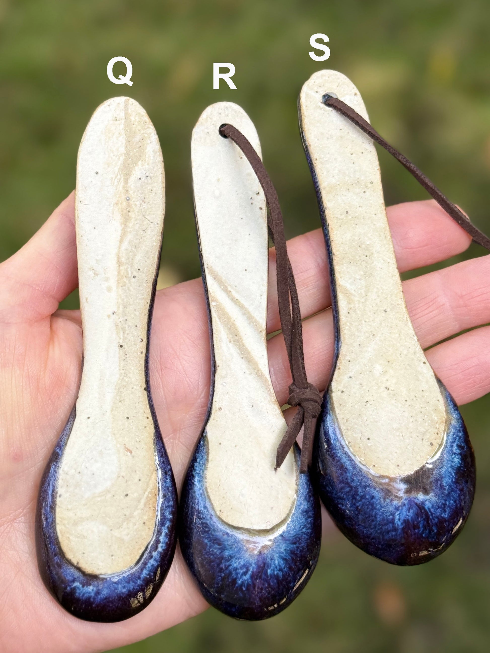 Three ceramic spoons with blue and white glaze held in a hand against a blurred green background.
